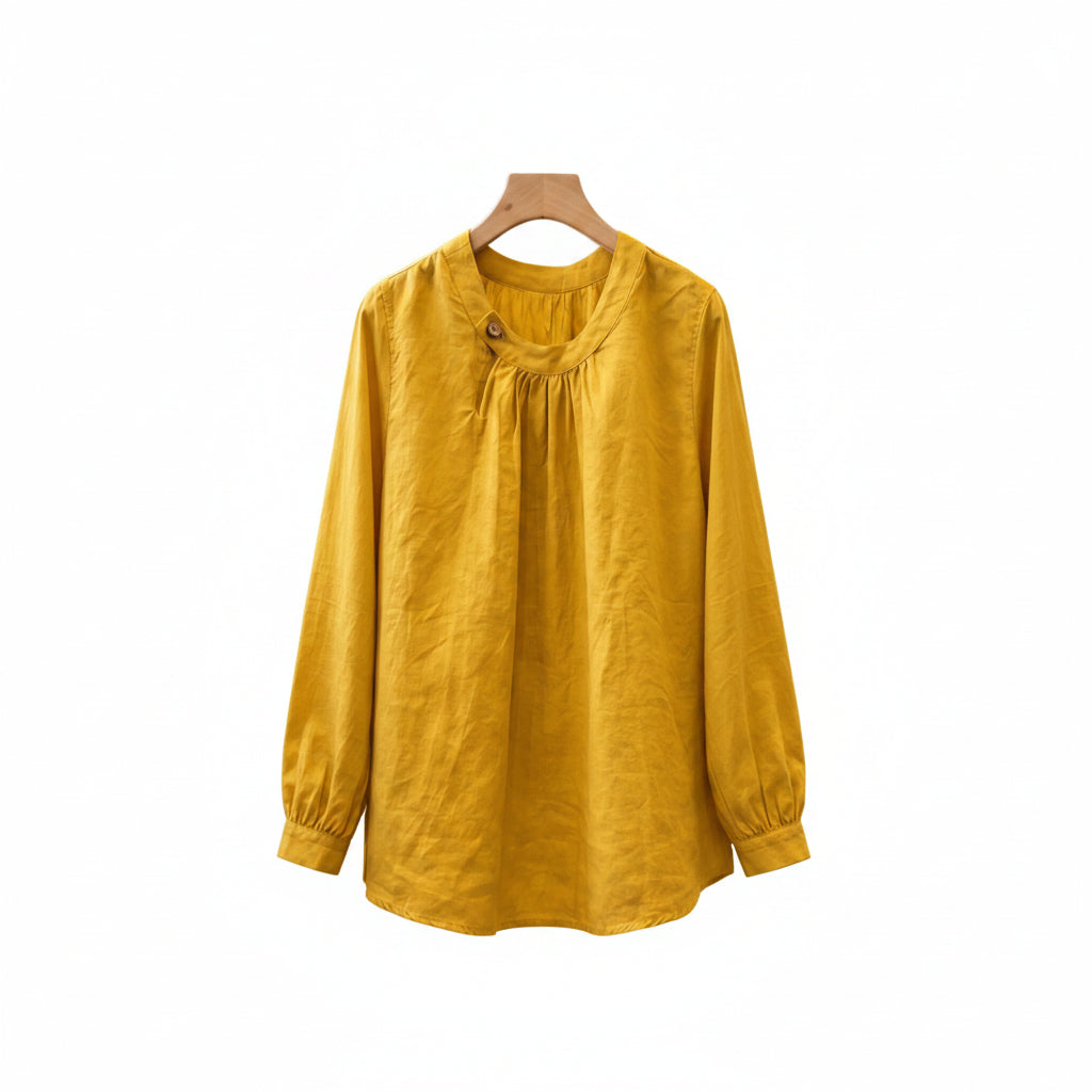 A mustard yellow long-sleeve linen blouse hanging on a wooden hanger in a rustic boutique setting.