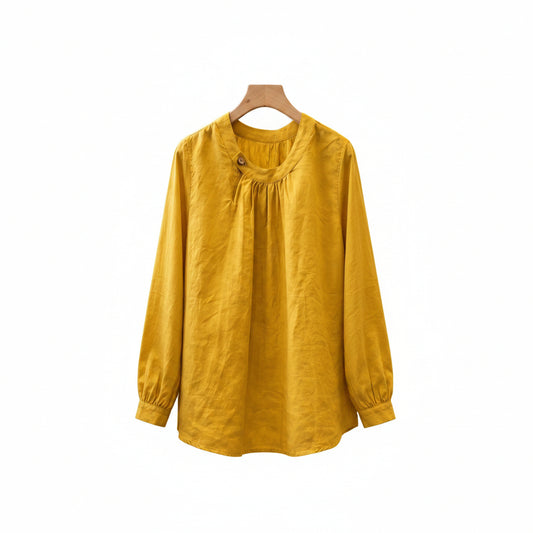 A mustard yellow long-sleeve linen blouse hanging on a wooden hanger in a rustic boutique setting.