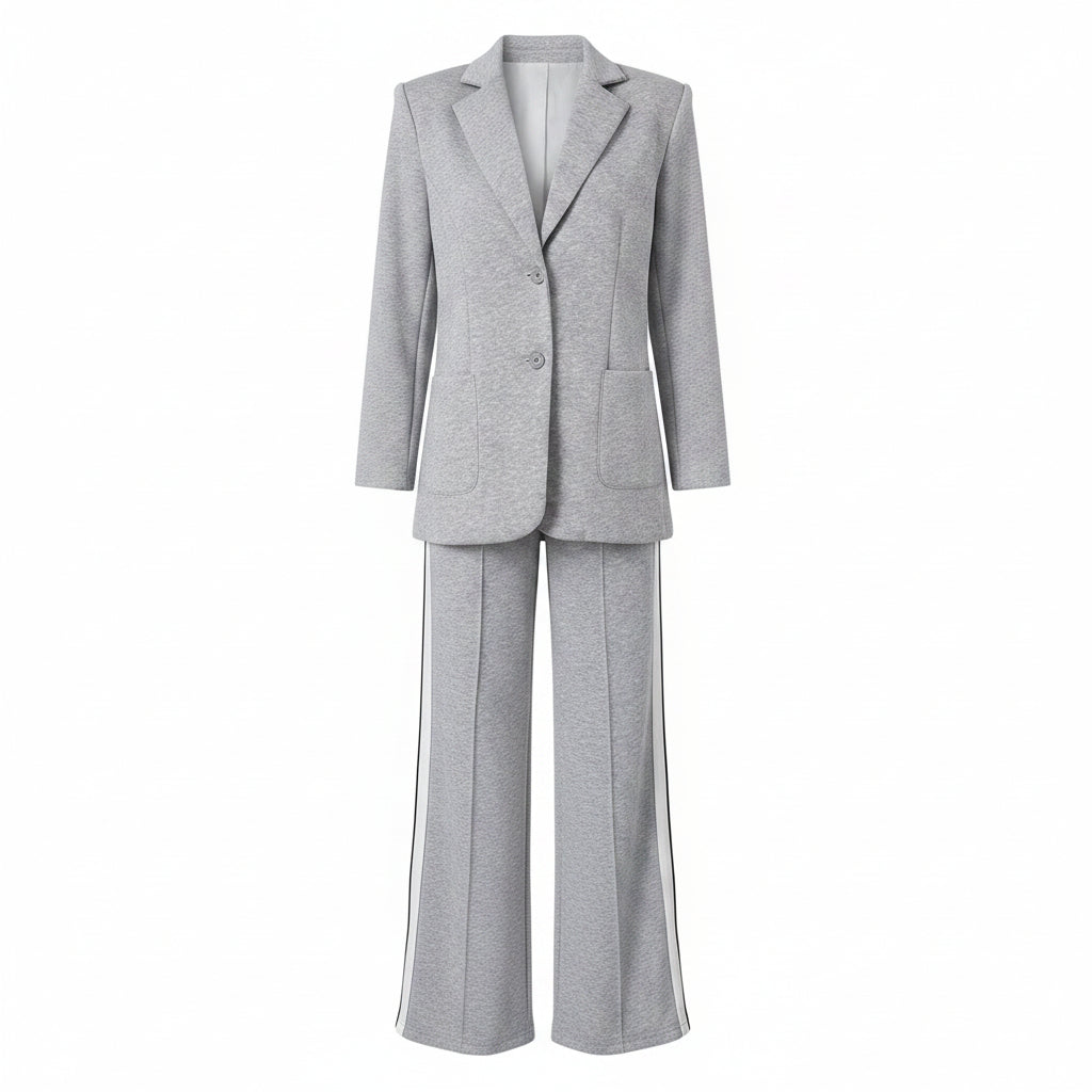 A woman models a light gray two-piece suit with white side stripes, featuring a blazer and matching wide-leg trousers, styled with a black top and a gray handbag in front of an open white closet.