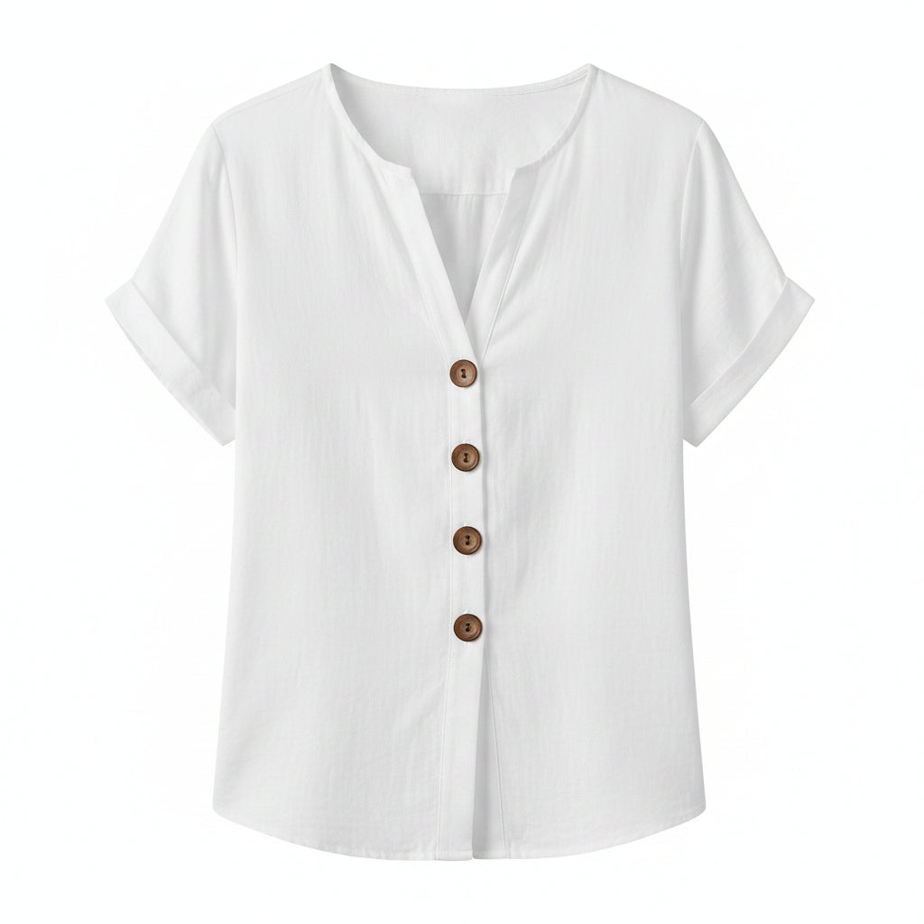 A woman wearing a white short-sleeve button-front blouse with brown buttons and light beige pants, styled with layered necklaces and bracelets in a warm indoor setting.