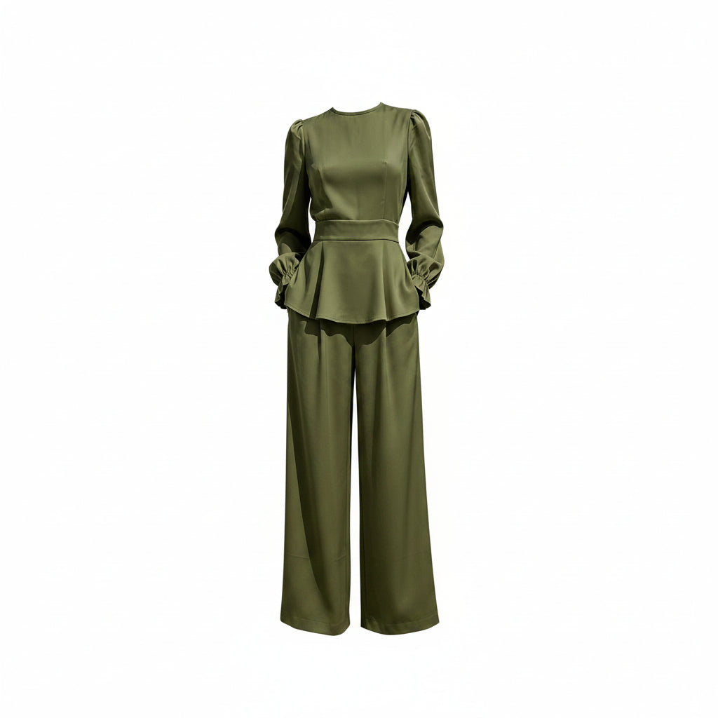 Person wearing a green outfit with a peplum top and wide-leg pants against a white marble wall.