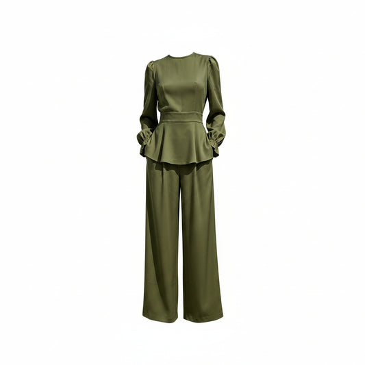 Person wearing a green outfit with a peplum top and wide-leg pants against a white marble wall.
