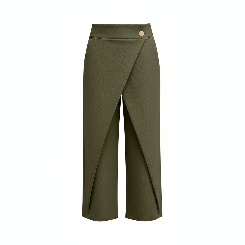 A model wearing olive green wrap-style cropped pants with a single gold button at the waist, paired with a white long-sleeve blouse and silver heels, against a solid gray studio background.