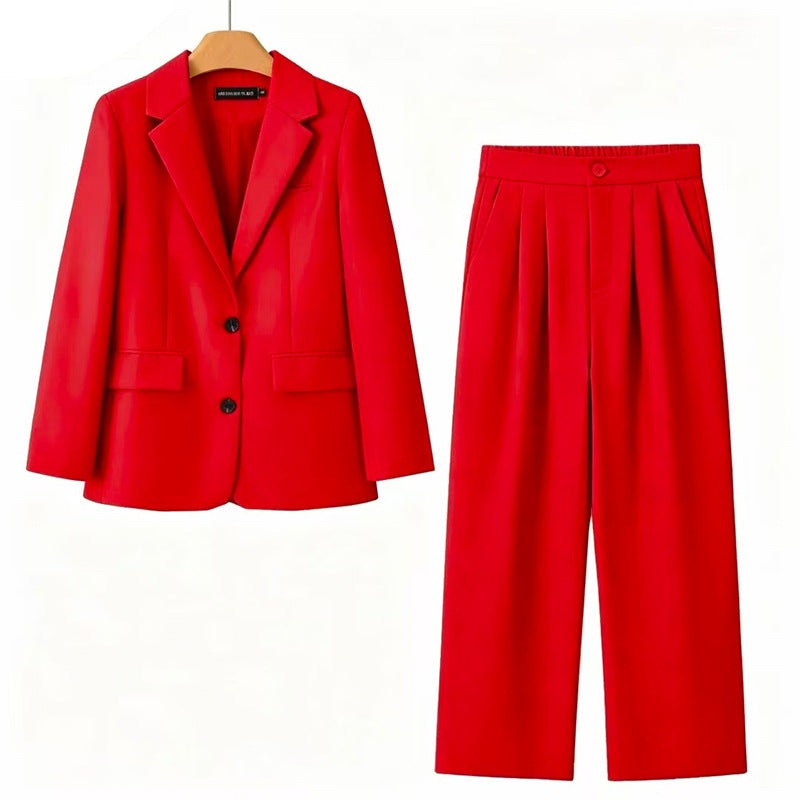 A bright red two-piece women's suit set consisting of a single-breasted blazer on a wooden hanger and matching pleated wide-leg trousers, displayed against a plain white background.