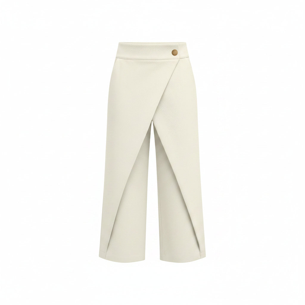 A model wearing off-white wrap-style cropped trousers with a single gold button at the waist, paired with a white long-sleeve blouse and pointed silver heels, against a solid gray studio background.