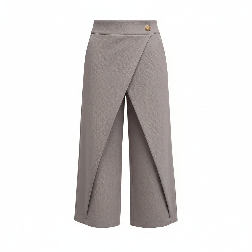 A model wearing a pair of high-waisted, wide-leg cropped trousers in a muted taupe-gray color, styled with a white long-sleeve blouse and clear high heels against a solid gray studio background.