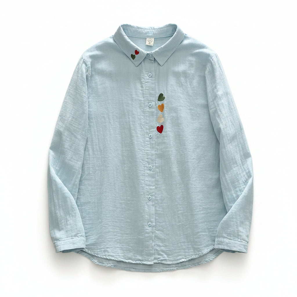 Light blue button-up shirt with colorful heart and rainbow design on a wooden surface