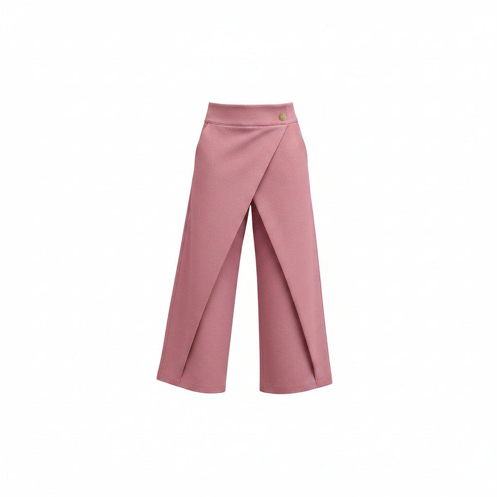 A model wearing a pair of pink wrap-style cropped pants with a single gold button at the waist, paired with a white long-sleeve blouse and silver heels, against a solid gray studio background.